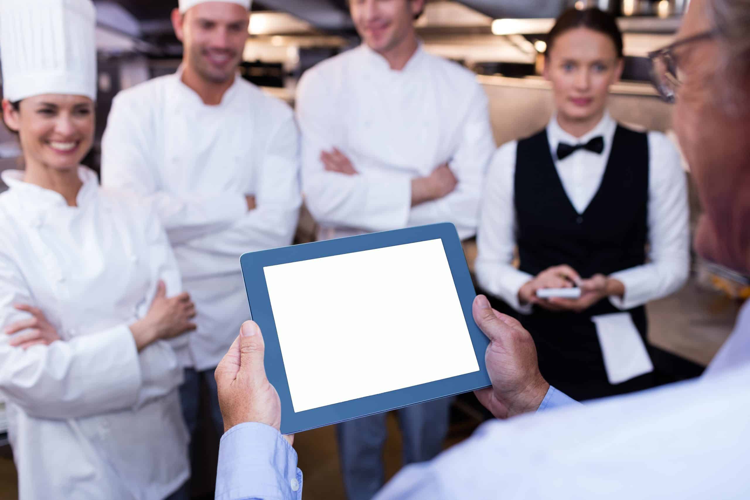 Chefs and staff discussing kitchen design with a tablet in a commercial kitchen.