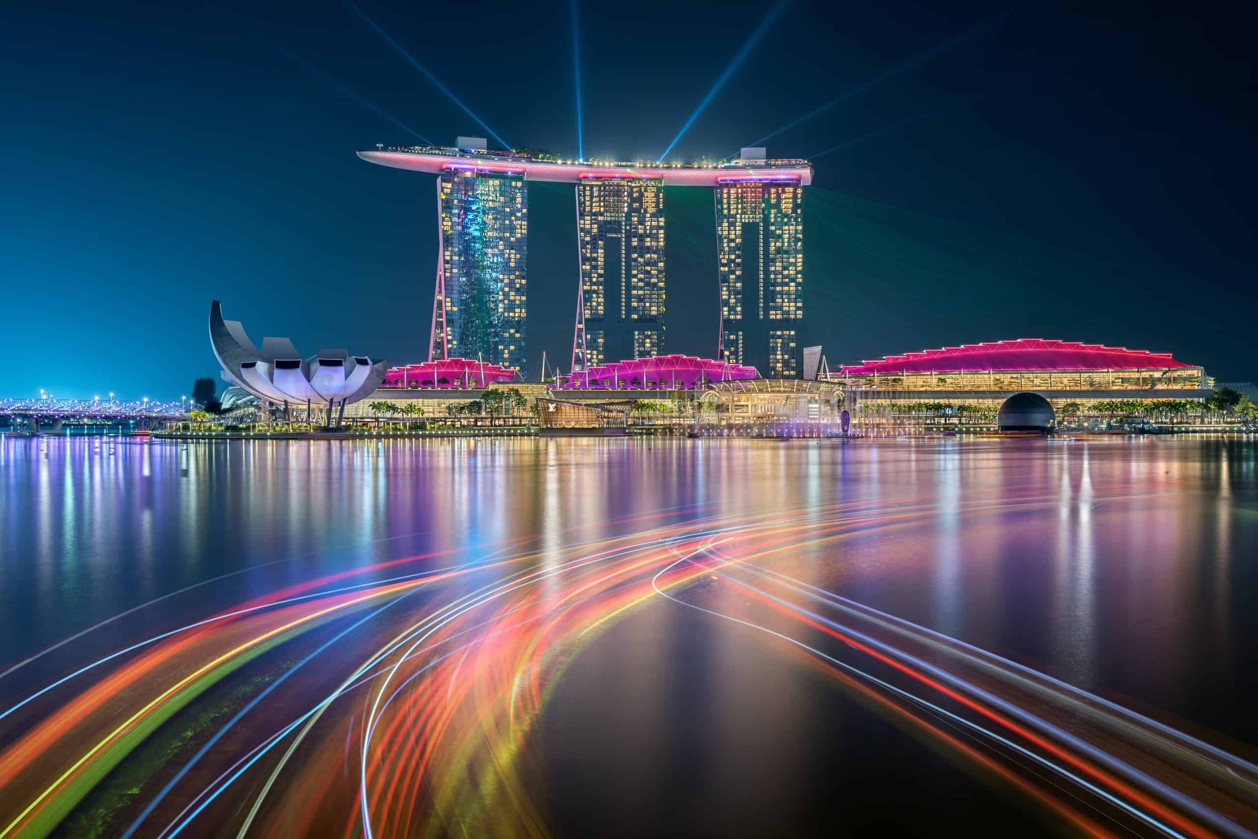 Vibrant night scene of Marina Bay Sands and Singapore skyline with colorful light trails.